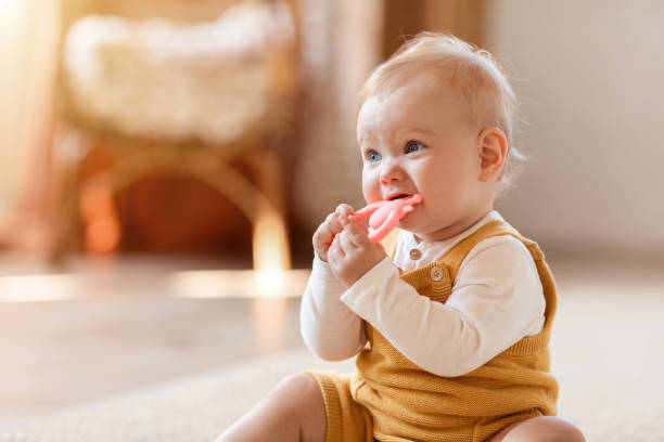 baby sitting on the floor while biting on a teething toy