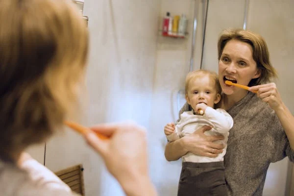  a woman holding a baby while brushing her teeth