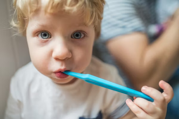 a little kid brushing his teeth with a blue toothbrush