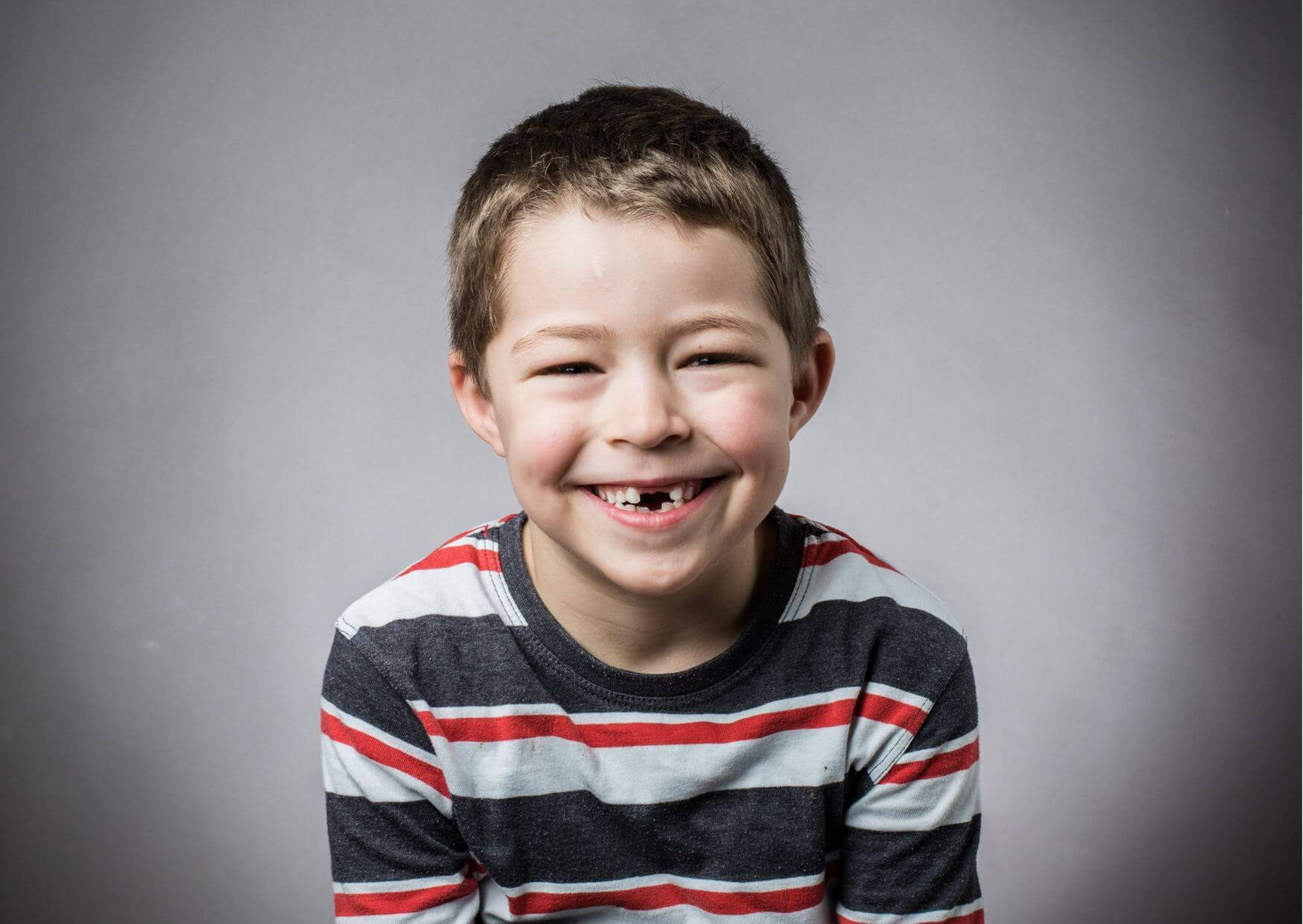 Smiling boy with a missing front tooth, showing the natural process of losing a first baby tooth and permanent teeth development.