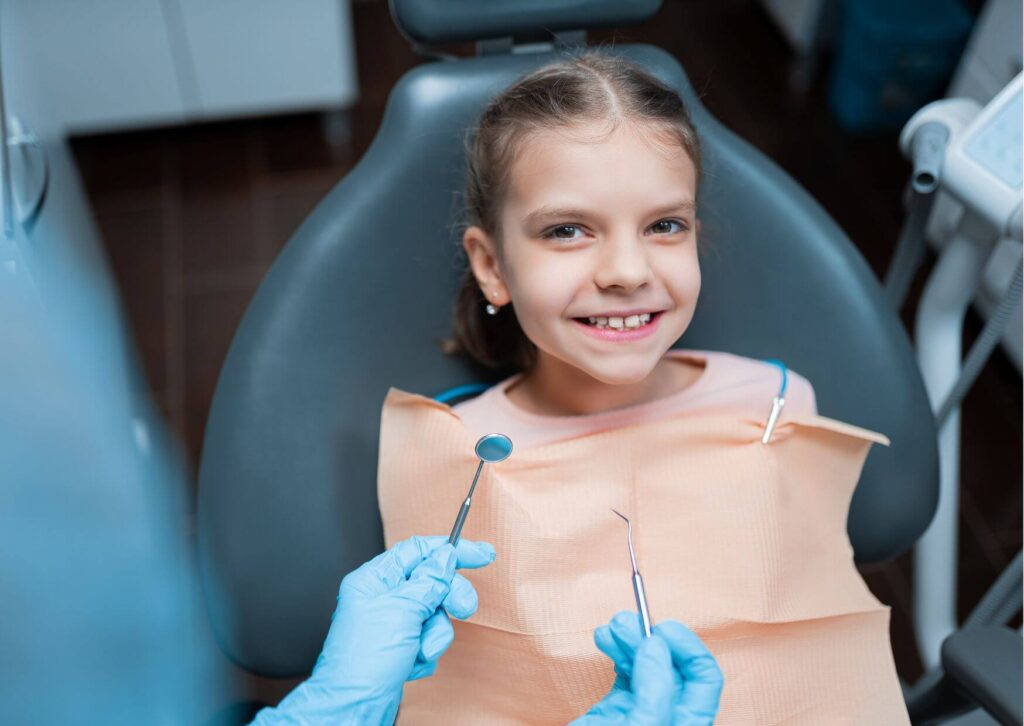 Young child smiling during a routine dental exam, highlighting the importance of taking children to the dentist for early preventive care.