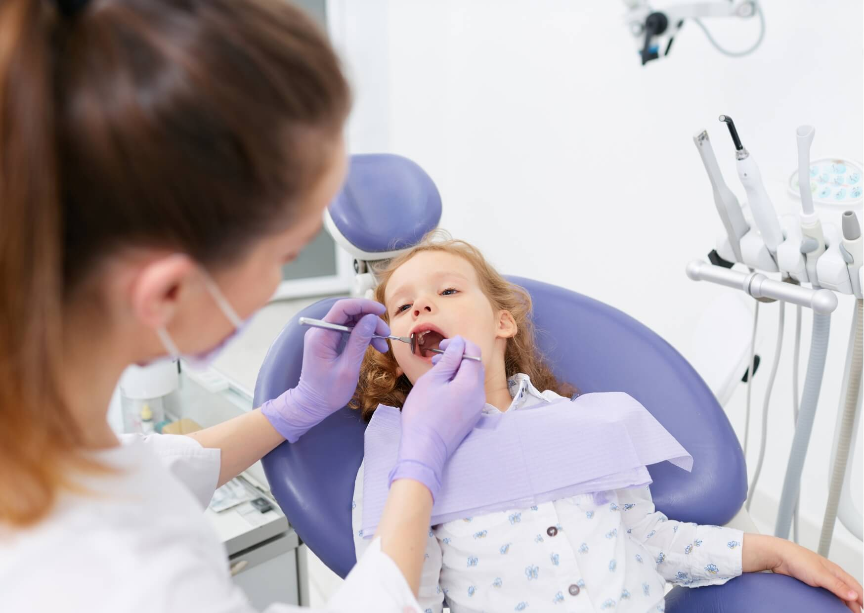 Dentist gently examining a young child's teeth during a routine checkup, illustrating how to prepare a child for a dental visit.