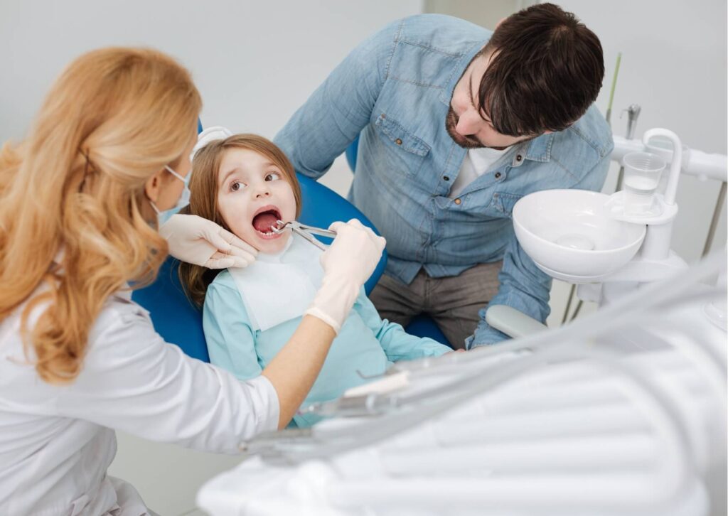 Pediatric dentist examining a child's teeth with a parent present during a visit to evaluate whether a kids dental spacer is needed after early tooth loss.