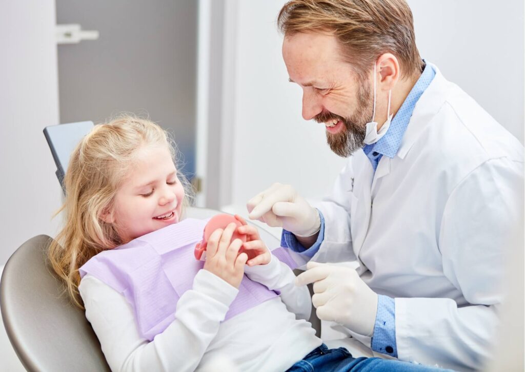 Pediatric dentist helping a young child feel comfortable by using a dental model while preparing a child for a dental visit.