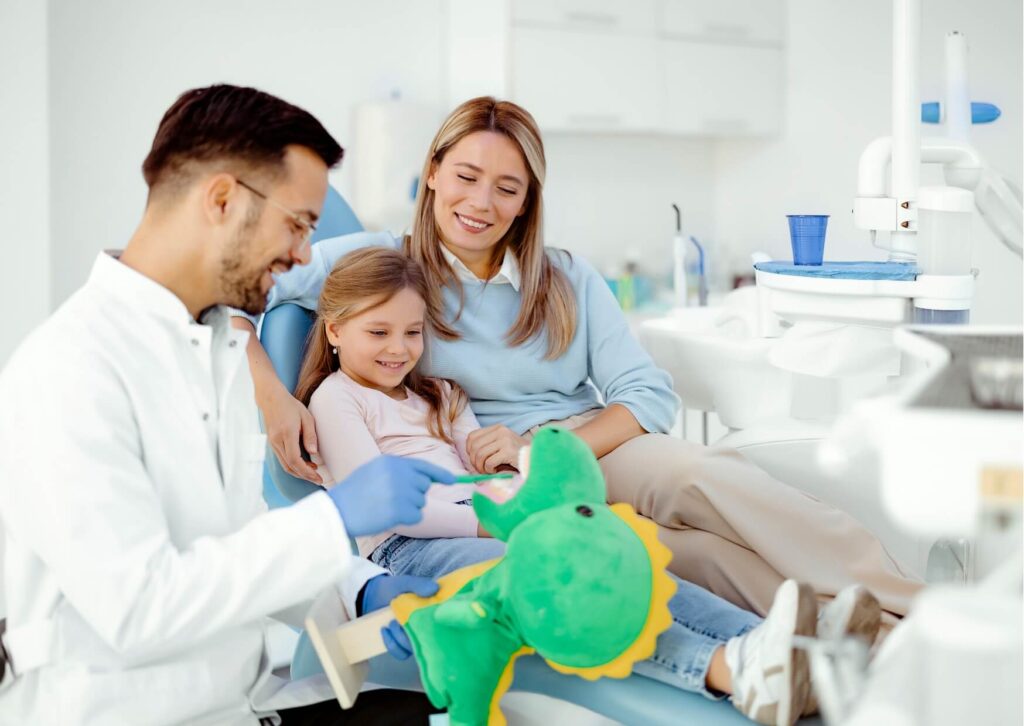 Pediatric dentist teaching a young child and parent about oral care after kids lose their first tooth during a dental visit.